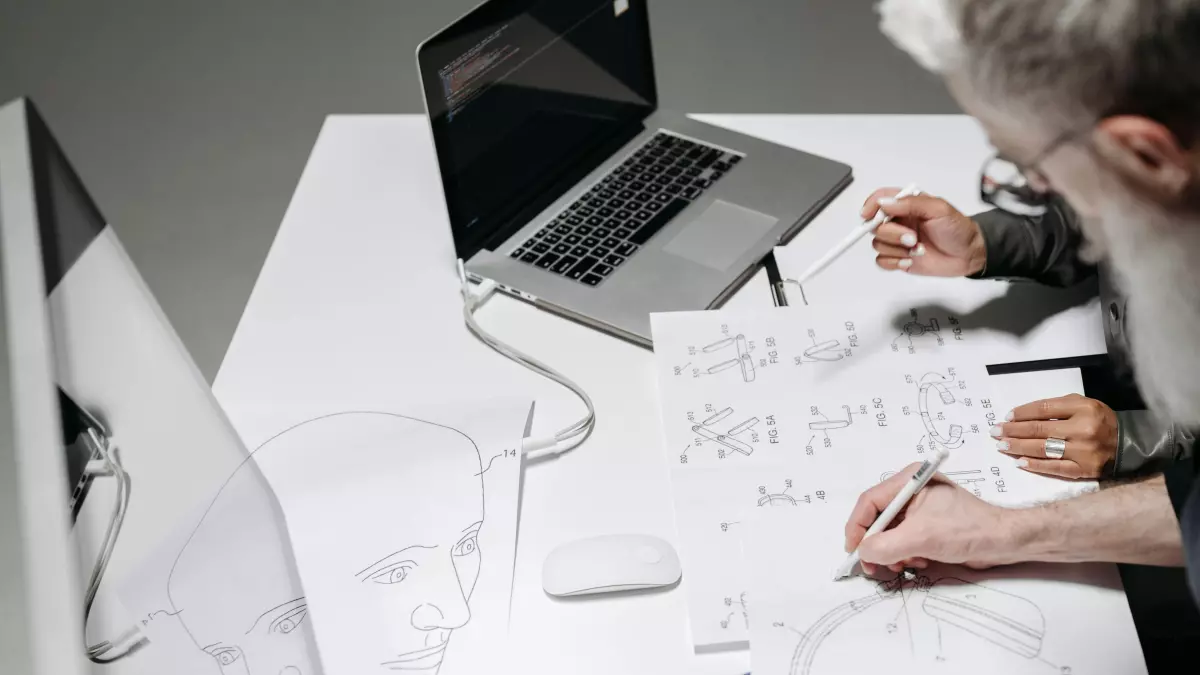 Two people are working together on a diagram at a desk with a laptop and other office supplies.